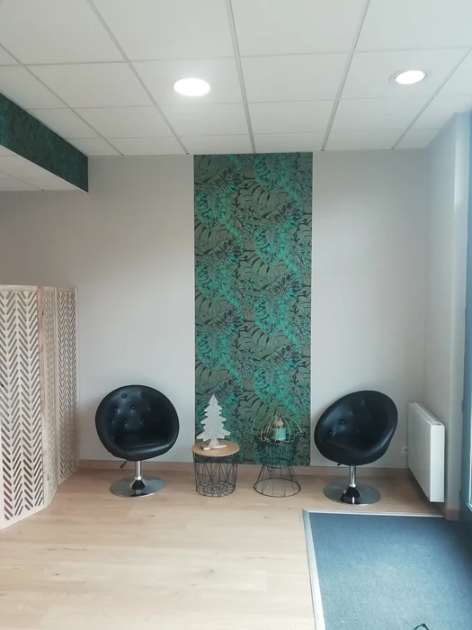 Espace d'accueil moderne avec deux fauteuils pivotants noirs face à face, séparés par tables basses design. Mur d'accent avec papier peint tropical vert émeraude, paravent décoratif à motifs géométriques blancs.