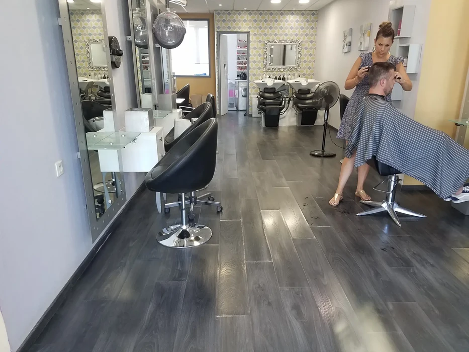 Intérieur d'un salon de coiffure moderne avec coiffeur homme travaillant sur client assis. Coiffeuse debout utilise des ciseaux pour couper les cheveux.