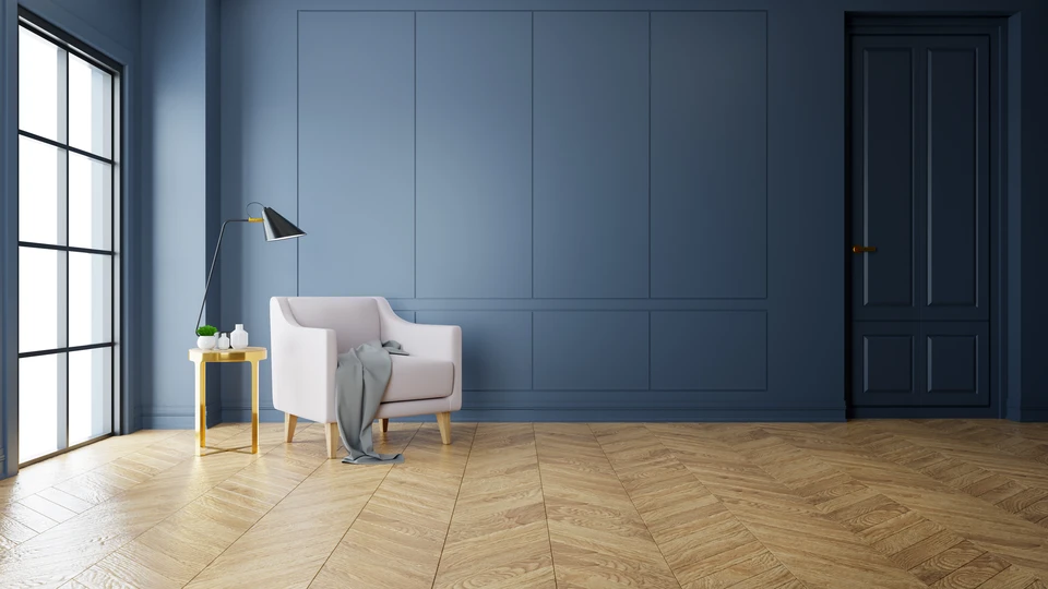 Intérieur résidentiel moderne avec fauteuil beige, parquet chevron chêne massif, mur lambris bleu marine, fenêtre verrière noire, lampadaire design métal noir et laiton, table d'appoint bois naturel. Espace salon épuré style contemporain.