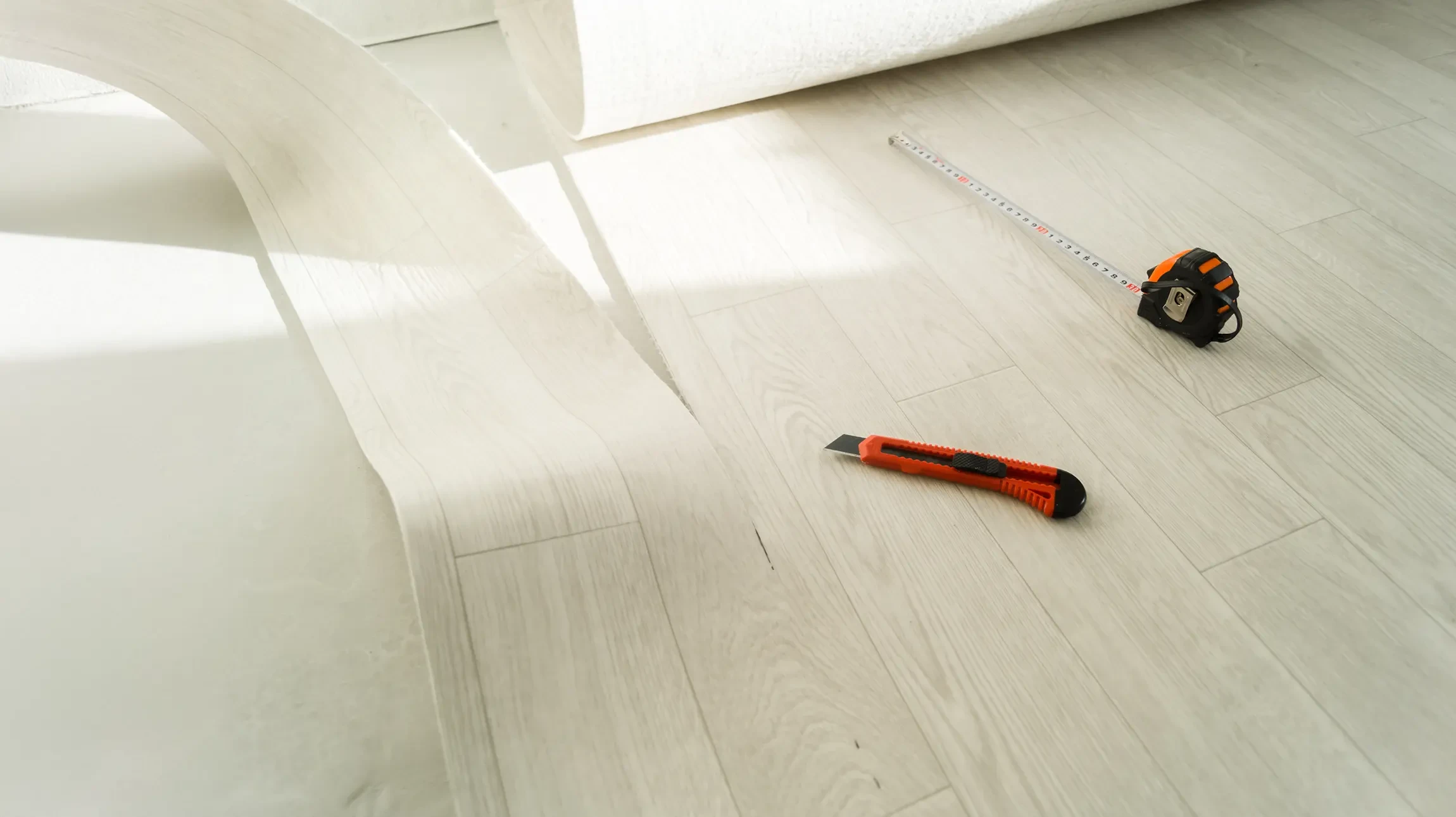 Intérieur moderne minimaliste avec fauteuil lounge en cuir noir et pouf assorti sur sol béton ciré. Murs blancs, grande plante verte en pot céramique beige, rideaux blancs. Ambiance contemporaine épurée.