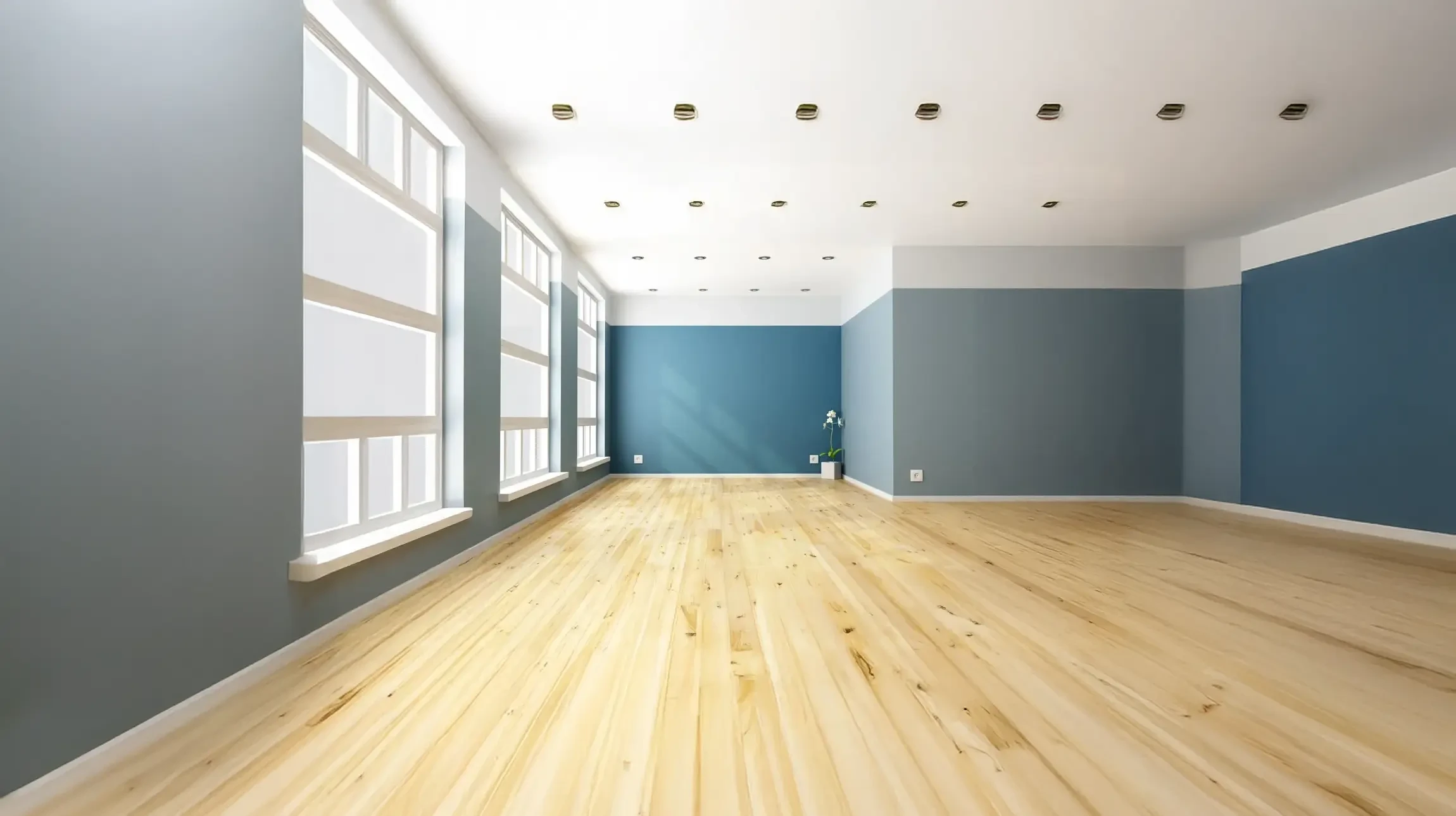 Salon moderne avec cheminée encastrée allumée et télévision murale intégrée dans mobilier blanc. Grande baie vitrée noire donnant sur jardin arboré. Plante verte décorative dans pot noir.